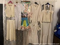 Full view of hanging costumes including clown costume, nurse dress, lab dress, cream trousers and vest, Annie Hall style blouse and underskirt