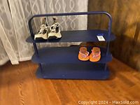 Front view of the blue metal shoe rack with two pairs of shoes displayed for size reference, set against wooden floor and drapes.