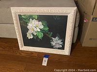 Framed floral artwork showing detailed white dogwood flowers and green leaves on branches with a dark background, in an ornate white frame.
