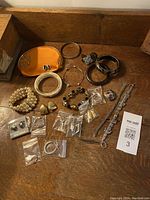 Full view of assorted bracelets and earrings alongside small orange pouch arranged on wooden surface.