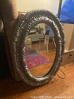 Front view of large oval mirror showing detailed ornate silver frame with floral and scroll embellishments.