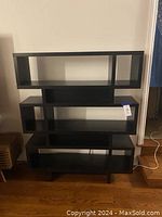 Front view of modern black bookcase with asymmetrical compartment design, showing five-tier shelves and 12 compartments including closed-back boxes