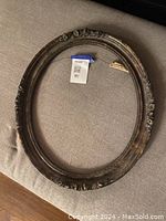Front view of an ornate oval frame with floral adornments on the outer edge and dark antique finish.