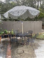 Full view of square patio table with four chairs set on patio including umbrella and umbrella stand.
