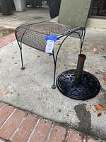 Metal mesh square patio table with four legs and black umbrella stand with decorative base and central pipe.