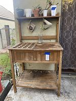 Front view of wooden planting bench showing slatted wood surface and interior plastic tray compartment, placed outside on patio.