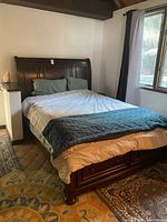 Front angle view of the queen bed showing the dark wood headboard and base with bedding on it.
