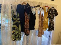 Full view of eight sundresses and rompers hanging on a curtain rod, showcasing patterns and colors including florals, solids, and lace details.