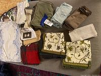 Photo showing assorted folded and rolled table linens arranged on a surface, including variety of cloth napkins, placemats, and tablecloths in different colors and patterns.