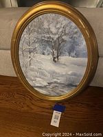 Oval framed winter landscape painting showing snow covered trees and creek with some frame wear.