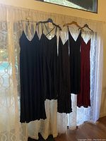 Four women's maxi dresses hanging on a curtain rod, three are black and one is red.