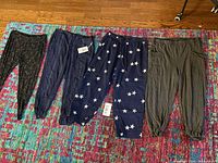 Photo showing four pairs of women's pants including two with star prints, one olive green, and one black printed pair.