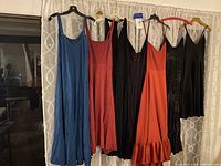 Front view of six women's dresses on hangers against a curtain background.