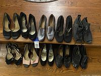 Full view of all 10 pairs of women's heels and shoes in various styles and colors arranged in two rows on wooden floor.