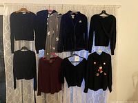 Full view of 8 women's long sleeve tops, including cardigans, hoodies, and sweaters, all size large, hanging on a curtain rod.