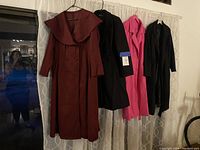 Four women's overcoats hanging on a curtain rod including brown, two black, and bright pink coats.