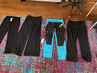 Four pairs of women's pants in size 12 arranged on a colorful rug, showing a variety of styles and colors including black dress pants and blue outdoor pants.