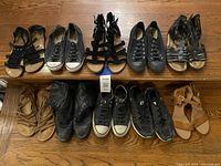 Lot of women's shoes displayed on a wooden surface including Converse sneakers, leather/boots, and various sandals.