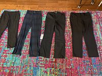 Four pairs of women's slacks/trousers laid out on a colorful rug showing color and style variety including solid black and plaid.