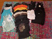Top-down photo showing a variety of women's tank tops and T-shirts in different colors and designs laid out on a red patterned carpet.