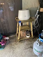 Front-left angled view of the yellow wheeled cart showing all three shelves and the wheels. The cart has a white appliance on top which is excluded from the lot.