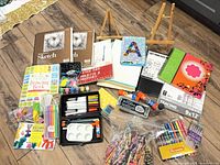 Full layout of art supplies showing sketch pads, notebooks, markers, gel pens, crayons, easels, paint set and accessories