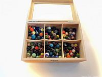 Top view of open wooden box showing six compartments filled with multicolor glass marbles