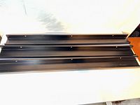 Three black IKEA RIBBA picture ledges laid flat, full view