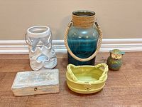 Group shot of five décor pieces: teal glass jar vase, white ceramic lantern, green ceramic basket dish, small owl figurine, carved wood box