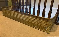 Full angled view of brass fender showing lattice sides and claw foot corner