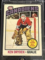 Front of 1976-7 O-Pee-Chee Ken Dryden Montreal Canadiens hockey card showing the player in goalie pose with team logo and 1st Team All Star badge