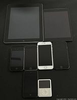 Full lot photo showing 2 iPads, 5 iPhones, and 1 iPod nano on black surface