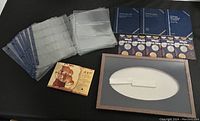 Photo showing multiple coin holder sheets, coin albums, and a currency display or folder with a vintage ship illustration