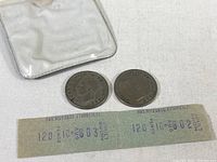 Two 2 Shilling coins accompanied by two vintage transit tickets inside a clear vinyl pouch on a white background.