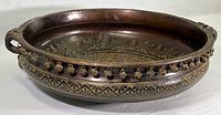 Full view of the 18 inch diameter traditional bronze Urli bowl with rich patina and etched designs inside, showing two scrolled handles and decorative bells on rim.