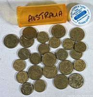 Photo of multiple Australian coins laid out with orange container labeled Australia and a white bottle cap for size reference.
