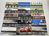 Overview of all 15 sealed Royal Mail mint stamp sets, arranged on flat surface showing original sealed packaging with thematic artwork and visible stamps