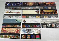 Overview photo showing eleven Royal Mail mint stamp collector sets in original packaging arranged flat, each with different thematic covers and visible stamps placed below thematic art.