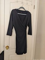 Full view of black Ann Taylor wrap dress hanging on hanger showing style and length.