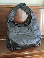 Front view of black leather purse showing overall shape, leather texture, and wide strap.