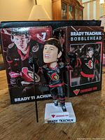 Brady Tkachuk bobblehead figure in full Ottawa Senators uniform with hockey stick, in front of packaging box.