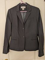 Front view of gray pinstripe blazer on hanger, showing two-button closure, two front pockets, and notched lapels.