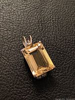Close-up photo of rectangular cut citrine gemstone pendant set in sterling silver on a black textured background.