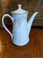 Side view of white coffee pot showing floral pattern, gold trim, handle and spout