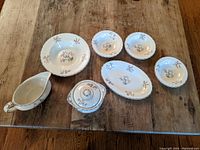 Photo showing the full set of English china including plates, bowls, a gravy boat, and a covered dish arranged on a wooden table.