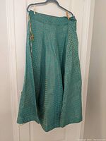 Full view of the long green skirt with gold circular patterns hung on a hanger