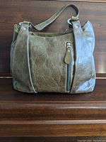 Full front view of olive green leather purse showing overall shape, strap, and front zippered pocket.