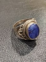 Sterling silver ring with ornate filigree and rope detailing around an oval cabochon blue quartz stone, shown against textured black background.