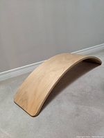 Curved wooden balance board resting on carpet, showing the full curved shape and smooth surface.