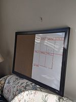 Photo of large framed board showing cork side and whiteboard side with weekly planner headings and grid.